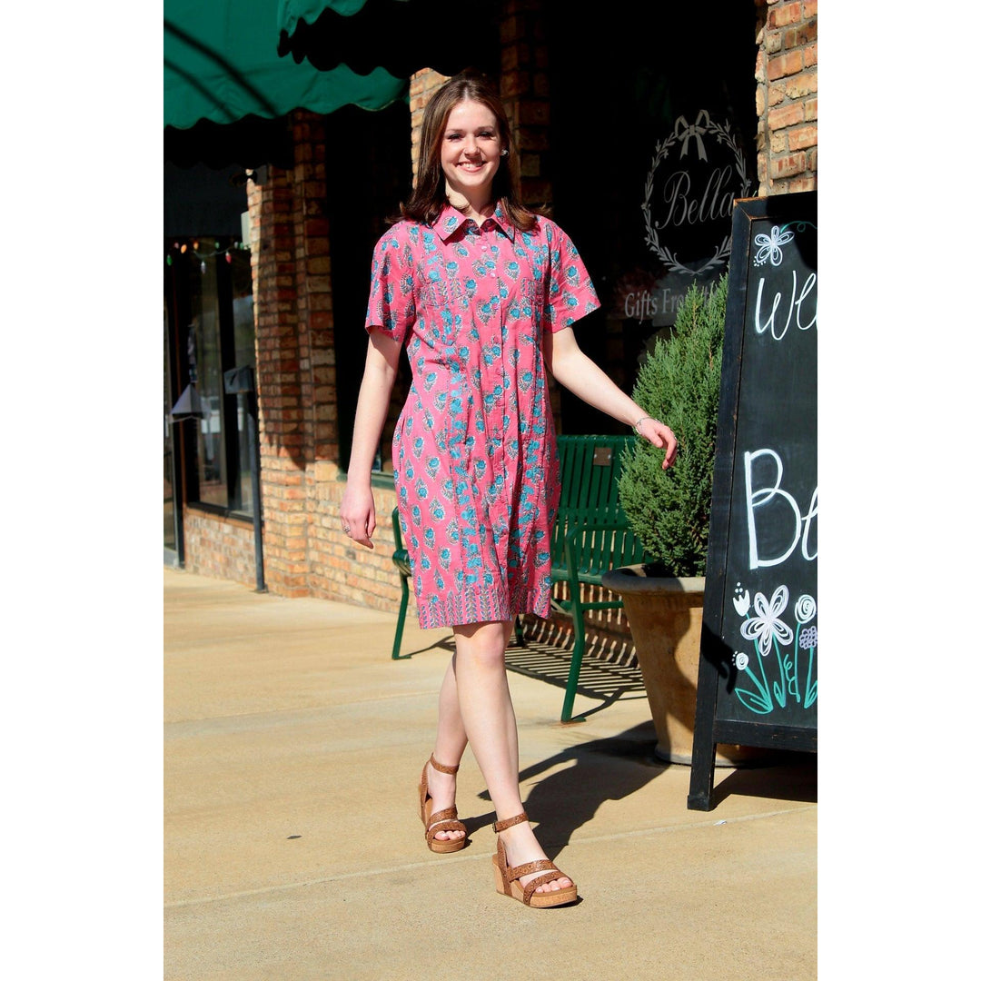 Young woman standing outdoors wearing a pink textured floral mini dress with a collar, paired with platform sandals.