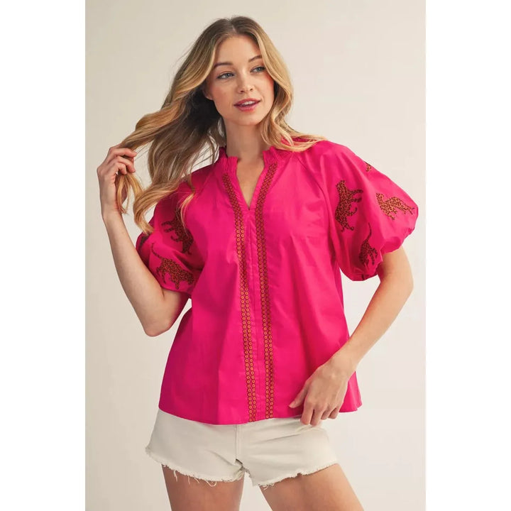 Woman wearing a pink blouse with embroidery on a plain background