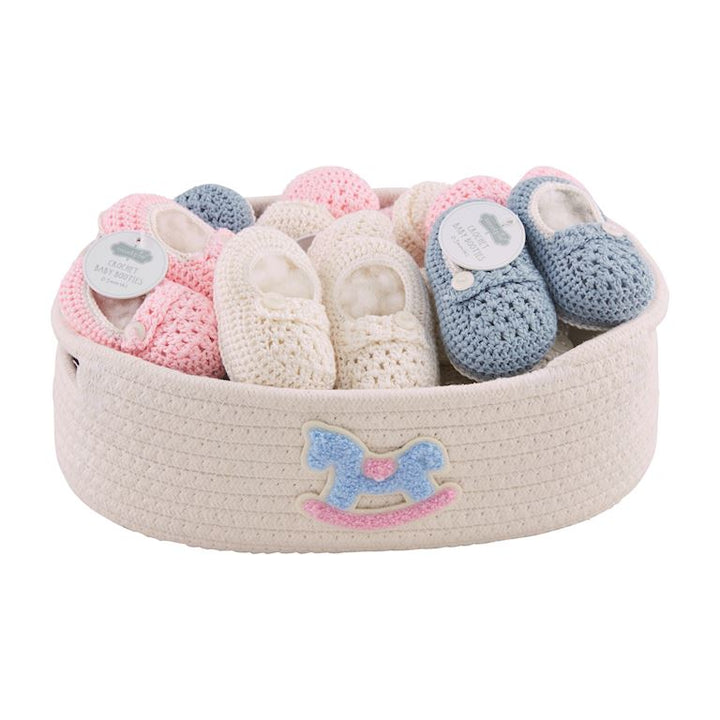 Assortment of Mud Pie crochet knit baby booties featuring button details in light blue, pink, and white, displayed in a cotton rope basket.