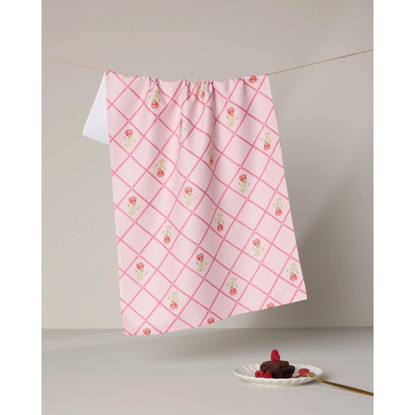 Pink and white checkered towel with floral patterns hanging on a line, with a dessert on a plate below.