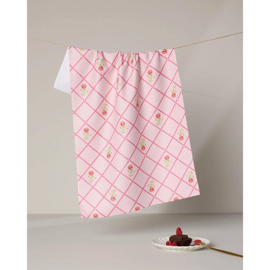 Pink and white checkered towel with floral patterns hanging on a line, with a dessert on a plate below.