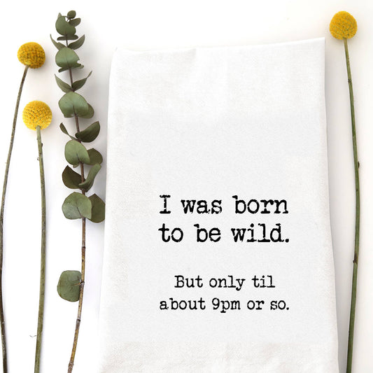 White cotton flour sack tea towel featuring the text "I was born to be wild. But only til about 9pm or so." in bold black lettering.