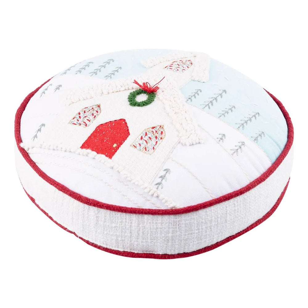 Glory Haus Round Christmas Church Pillow shown at an angle, showing the embroidered church front and the rounded side depth with red piping