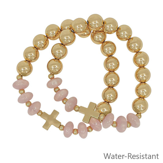 Gold and pink beaded bracelet with cross charms on a white background