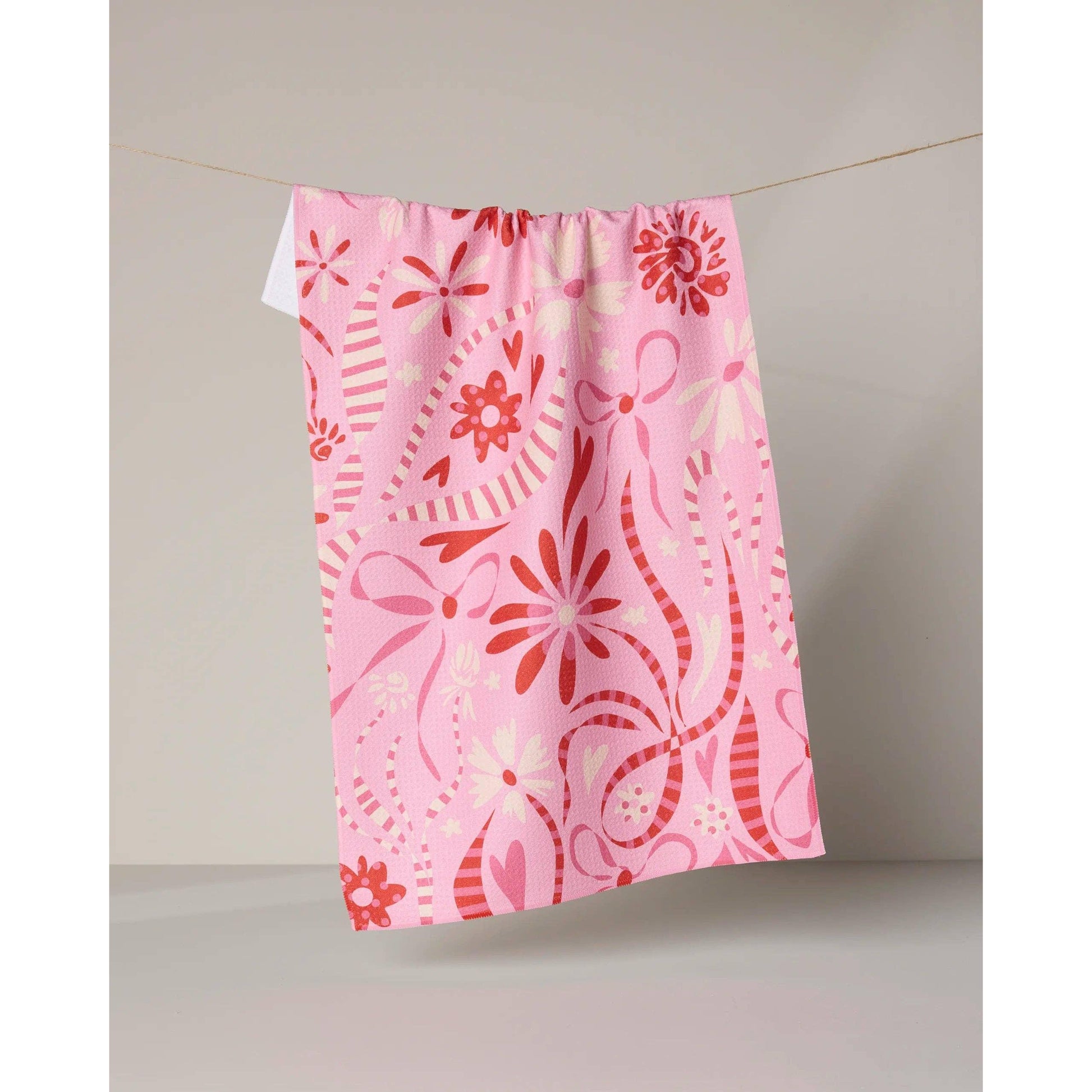 Pink towel with red floral and wavy patterns hanging on a line against a neutral background