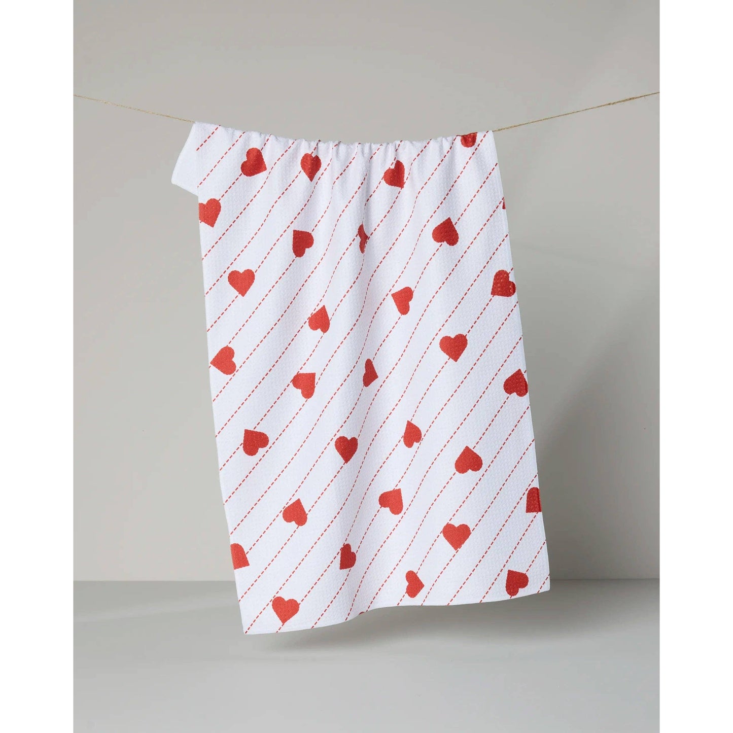 White towel with red heart pattern hanging on a line against a plain background