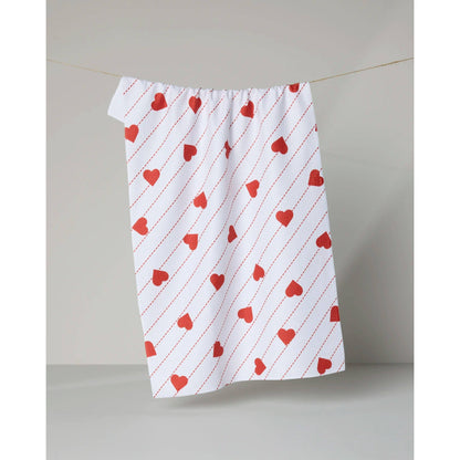 White towel with red heart pattern hanging on a line against a plain background