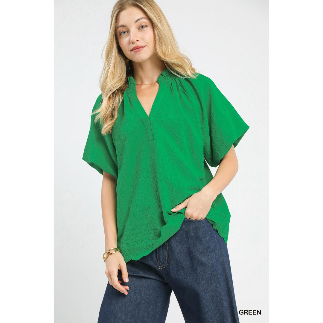 Woman modeling the Umgee Scalloped Hem Textured Blouse in vibrant green with ruffled collar, short puff sleeves, and scalloped hem.