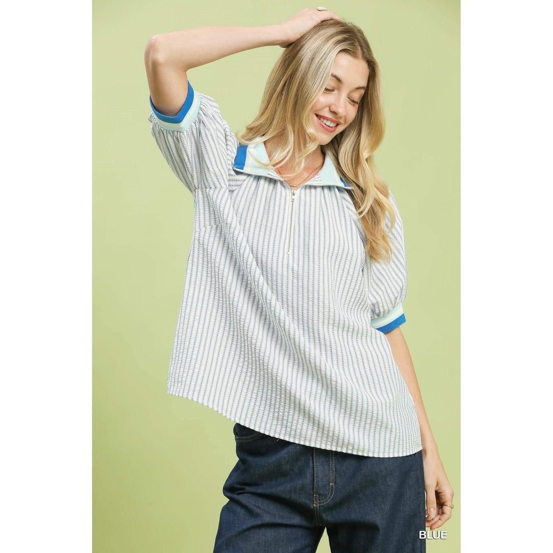 Woman modeling the Umgee Botanical Print Blouse in blue featuring a half-zip contrast collar, puff sleeves, and a relaxed boxy fit.