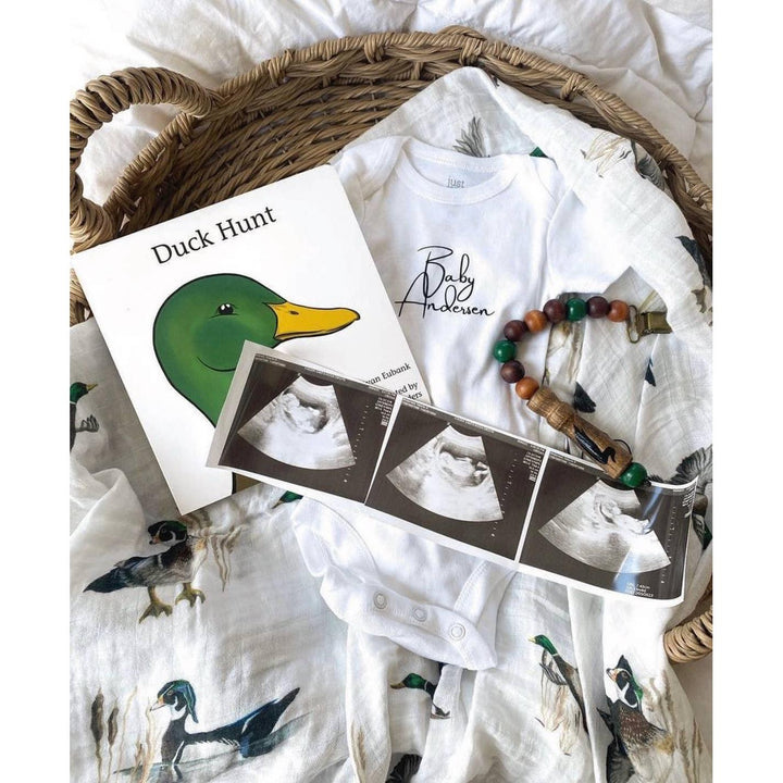 Lifestyle picture of duck hunt  book cover and baby ultrasound, along with duck swaddle and onesie