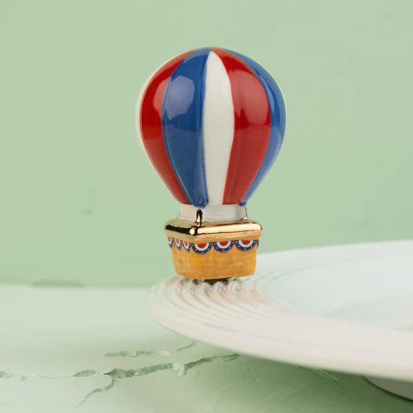 Nora Fleming Red, White, and Balloon mini featuring a patriotic hot air balloon with red and blue stripes and gold accents.