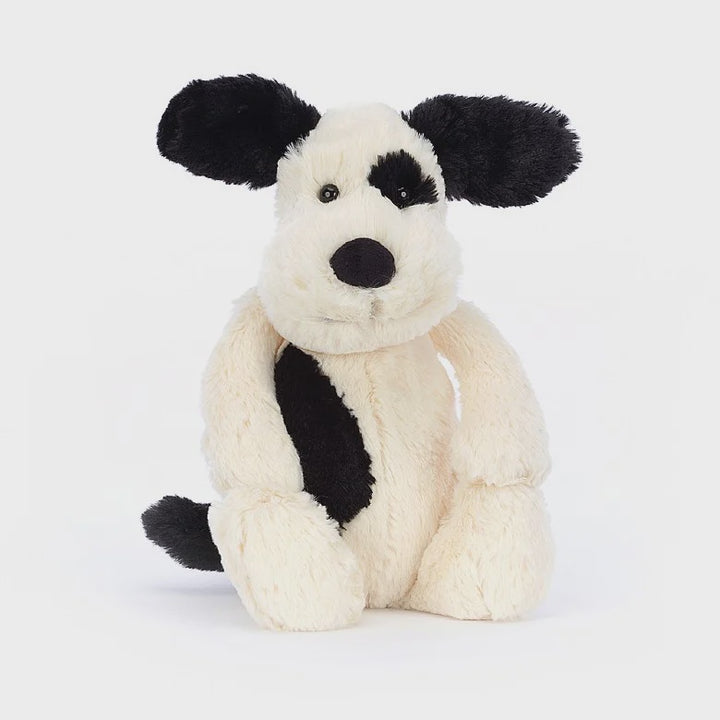 Cream-colored Bashful Puppy plush with black ears, tail, and eye patch by Jellycat.