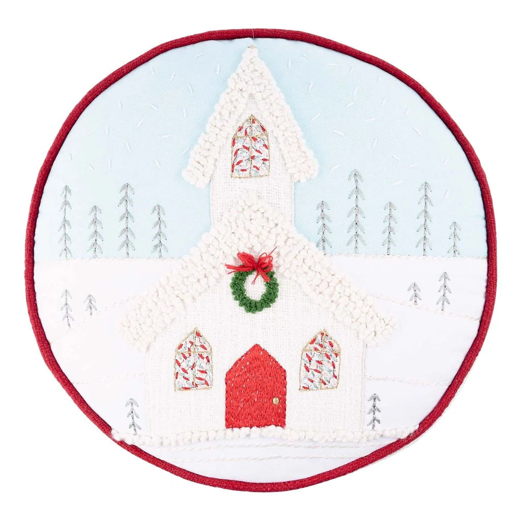Glory Haus Round Christmas Church Pillow, front — embroidered white church with red roof and door, wreath, and snowy winter scene on a red-piped round pillow