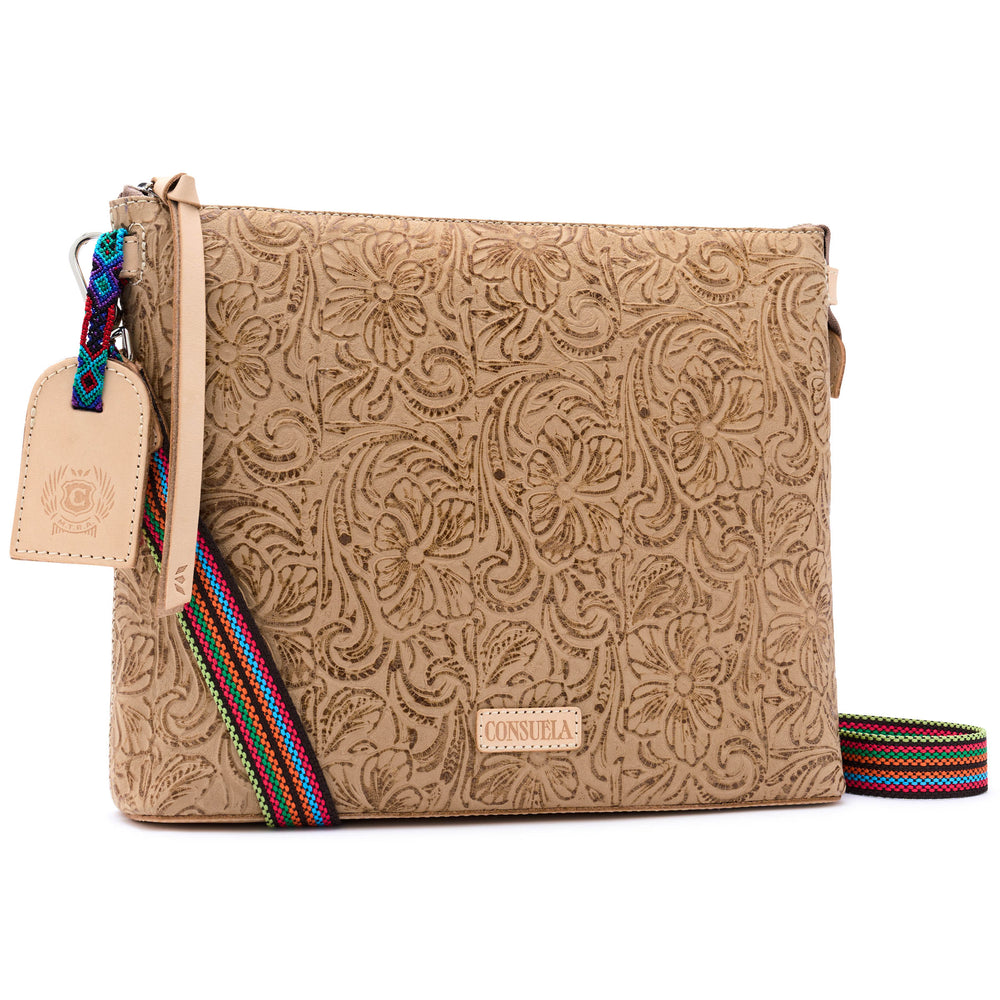 Consuela Lawton Downtown Crossbody in neutral tan tooled floral leather, three-quarter front view with a colorful woven strap and leather hangtag.