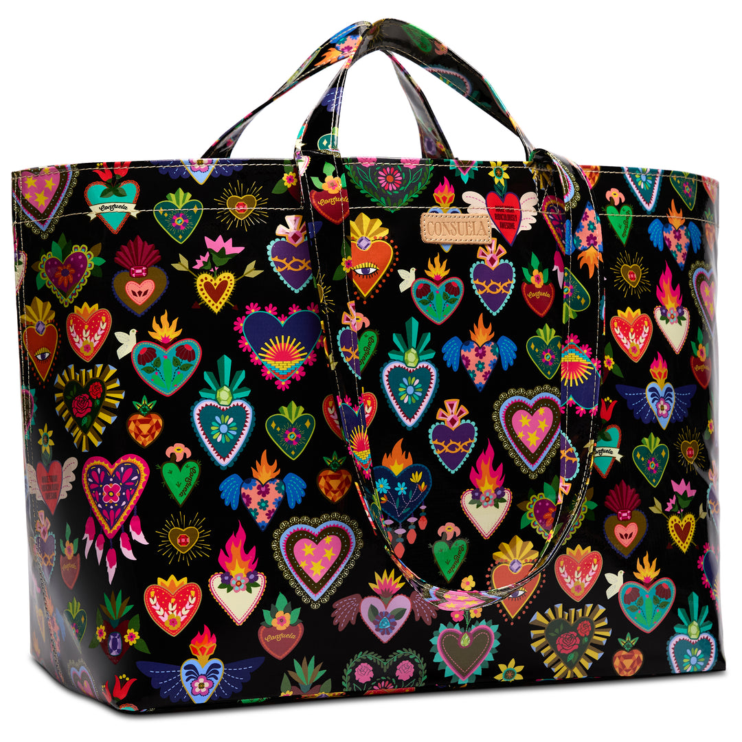 Three-quarter angled view of the Consuela Vida Grab n Go Jumbo, an oversized glossy black tote with an all-over colorful folk-art sacred-heart print and dual top handles.