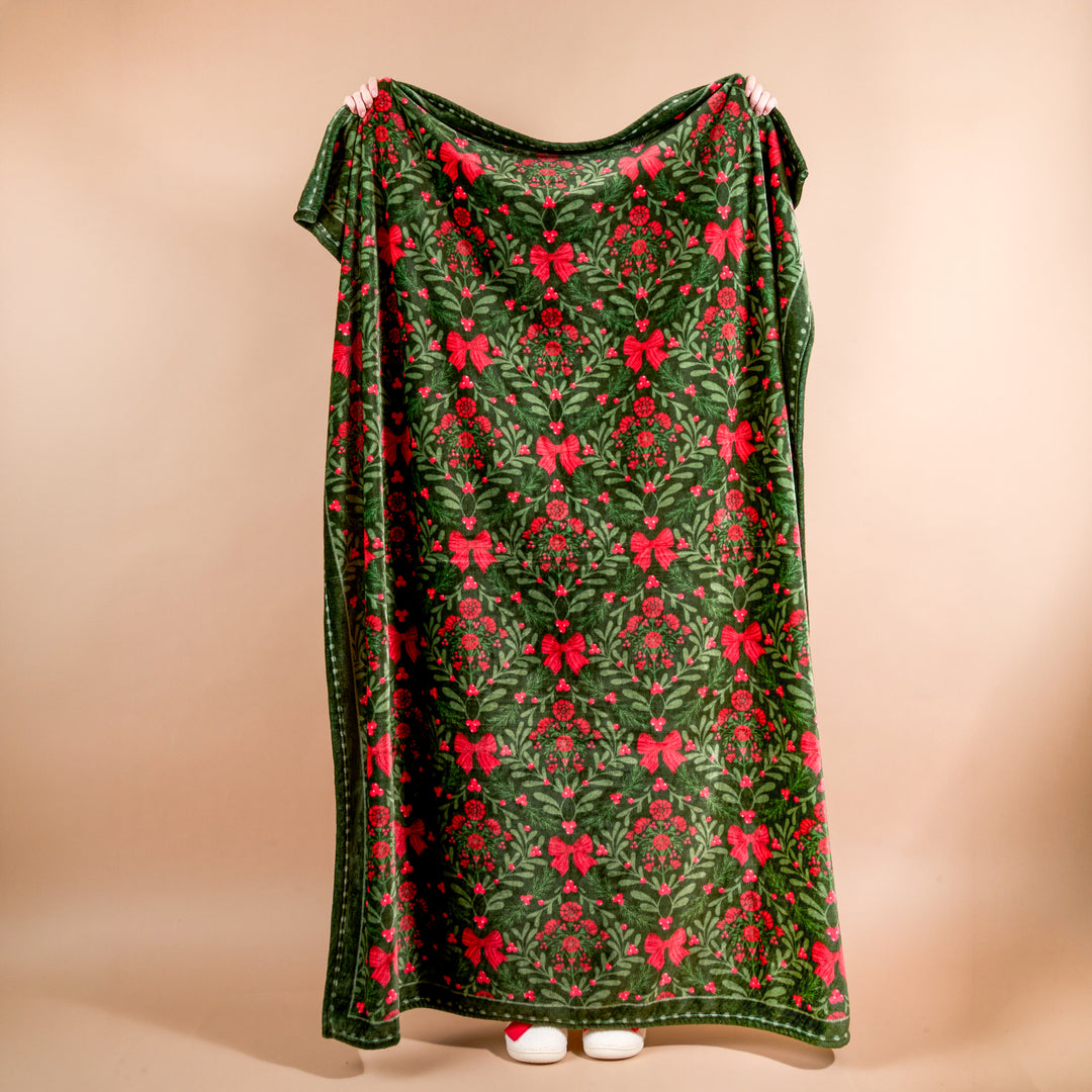 The Darling Effect Snuggle Up Plush Blanket draped to show the festive green and red A Merry Moment floral holiday print.