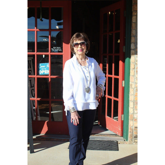 Woman standing in front of a red door with glass panels, wearing a white coat and sunglasses.