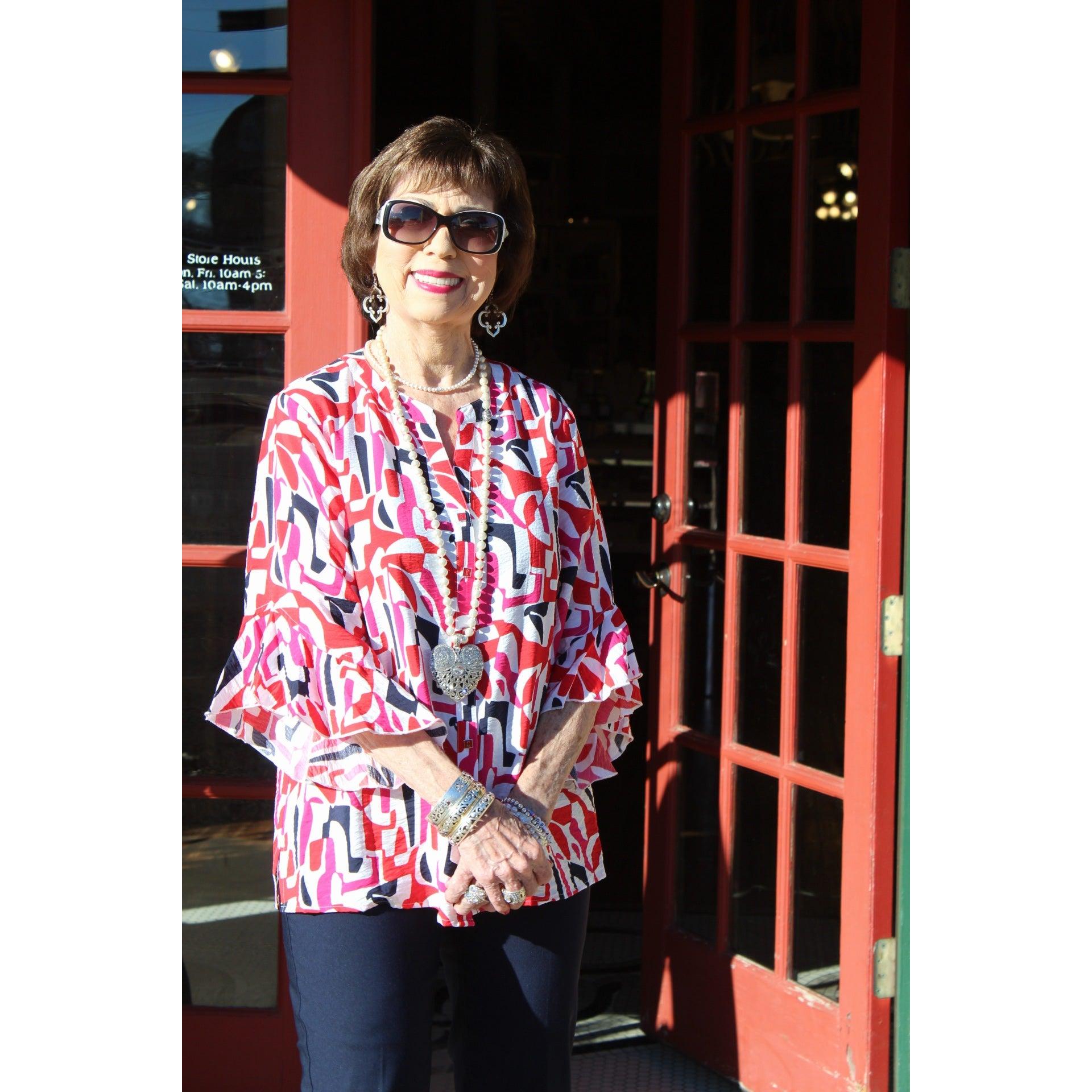 Woman in a colorful blouse standing next to a red door