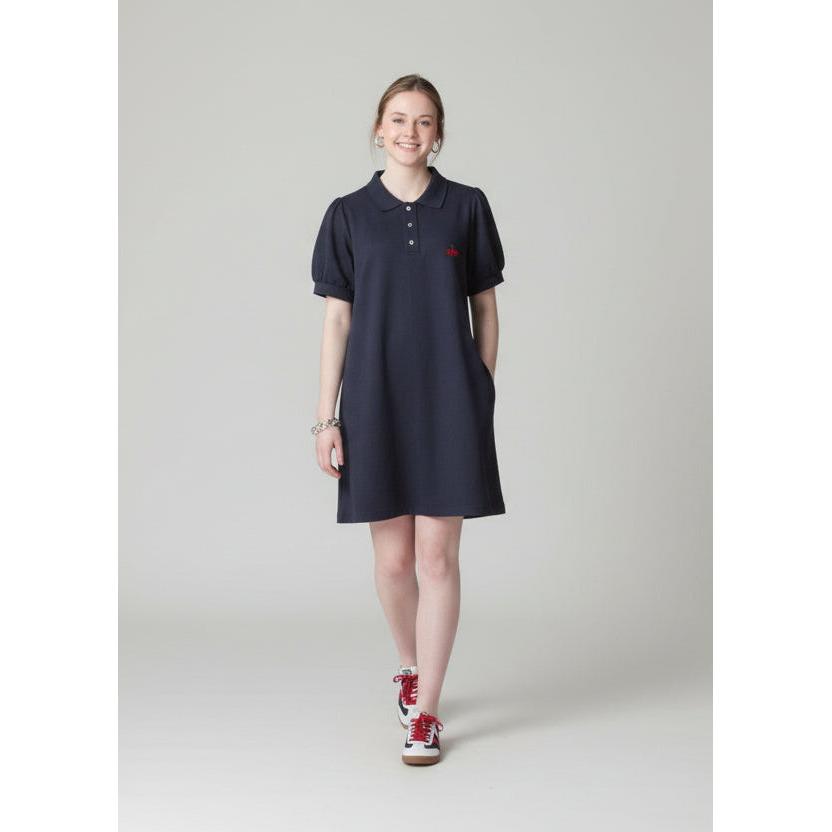 Person wearing a dark dress and red shoes standing on a sidewalk with brick steps and a store in the background.