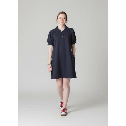 Person wearing a dark dress and red shoes standing on a sidewalk with brick steps and a store in the background.