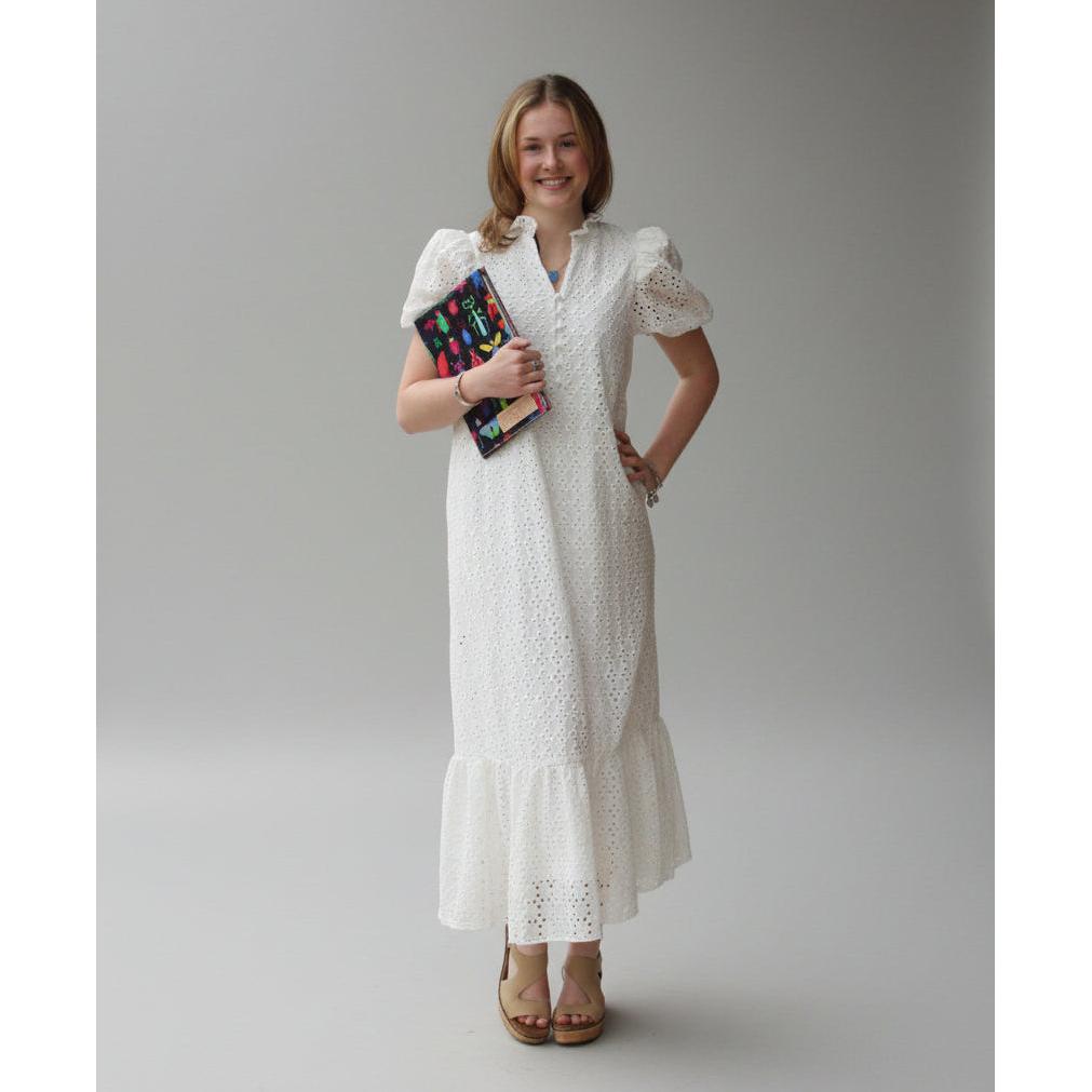 Woman wearing a white dress holding a colorful clutch against a plain background