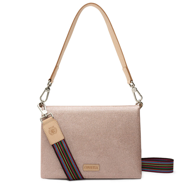 Consuela Emery Metro Crossbody in shimmering blush metallic glitter, front view with the flap closed, a natural leather strap, and a rainbow-striped woven crossbody strap.