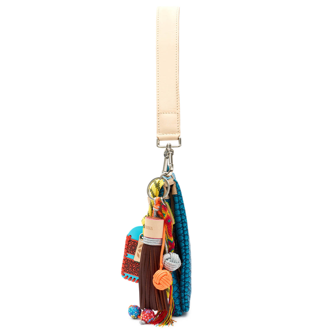 Side detail of the Consuela Indy Metro Crossbody with its multi-charm beaded and woven tassel hanging beside the teal bag.