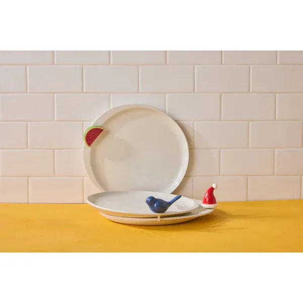 Nora Fleming Celebration Circle plate shown with a decorative heart mini inserted into the signature rim hole.