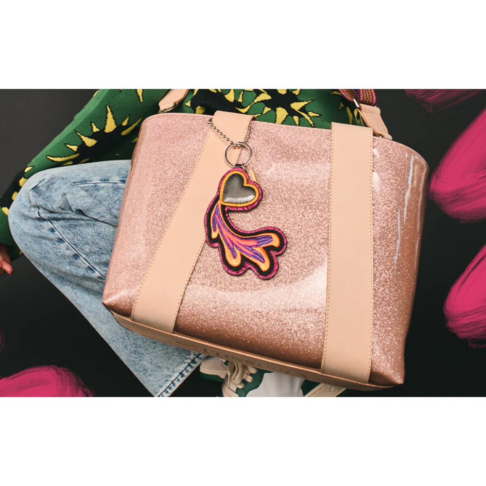 Consuela Emery Carryall featuring a champagne glitter exterior, natural leather handles, and a colorful woven crossbody strap.