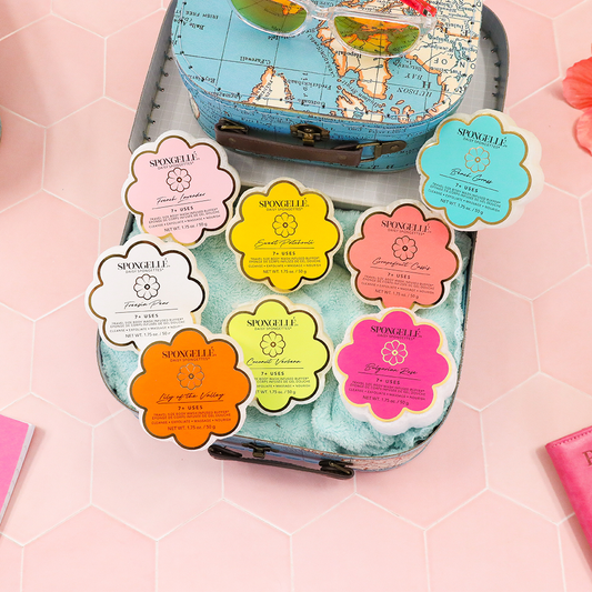 Assorted Spongellé Daisy Spongette flower-shaped soap buffers in a travel suitcase display