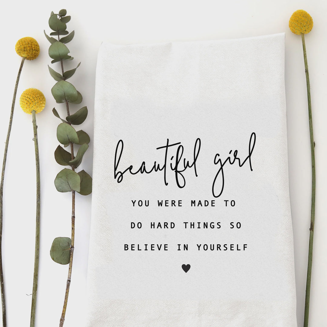 White cotton flour sack tea towel with the quote "Beautiful girl, you were made to do hard things so believe in yourself" in black script.