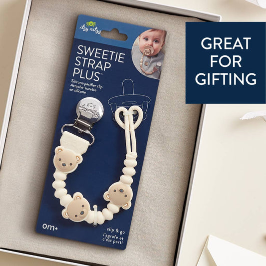 Baby pacifier clip with packaging on a beige surface, labeled 'Sweetie Strap Plus'.