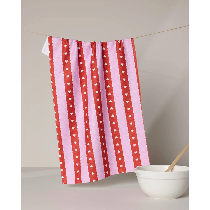Red and pink striped towel with heart pattern hanging on a line, next to a white bowl.