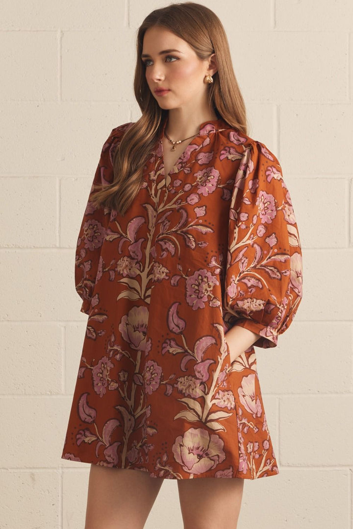 Model wearing the Entro Autumn Floral Mini Dress in Rust, featuring 3/4 puff sleeves, a V-neck, and side pockets.