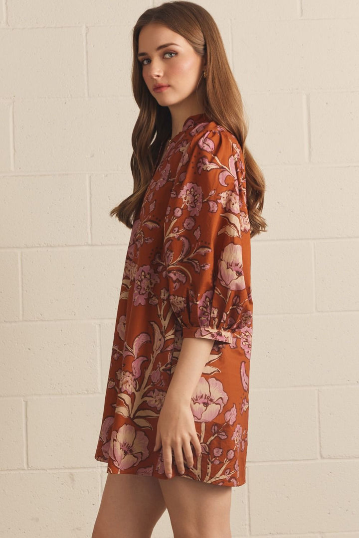 Model wearing the Entro Autumn Floral Mini Dress in Rust, featuring 3/4 puff sleeves, a V-neck, and side pockets.