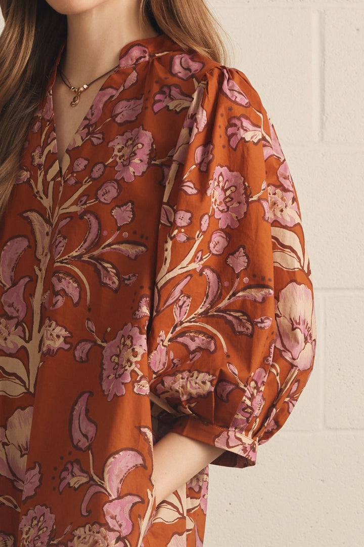 Model wearing the Entro Autumn Floral Mini Dress in Rust, featuring 3/4 puff sleeves, a V-neck, and side pockets.