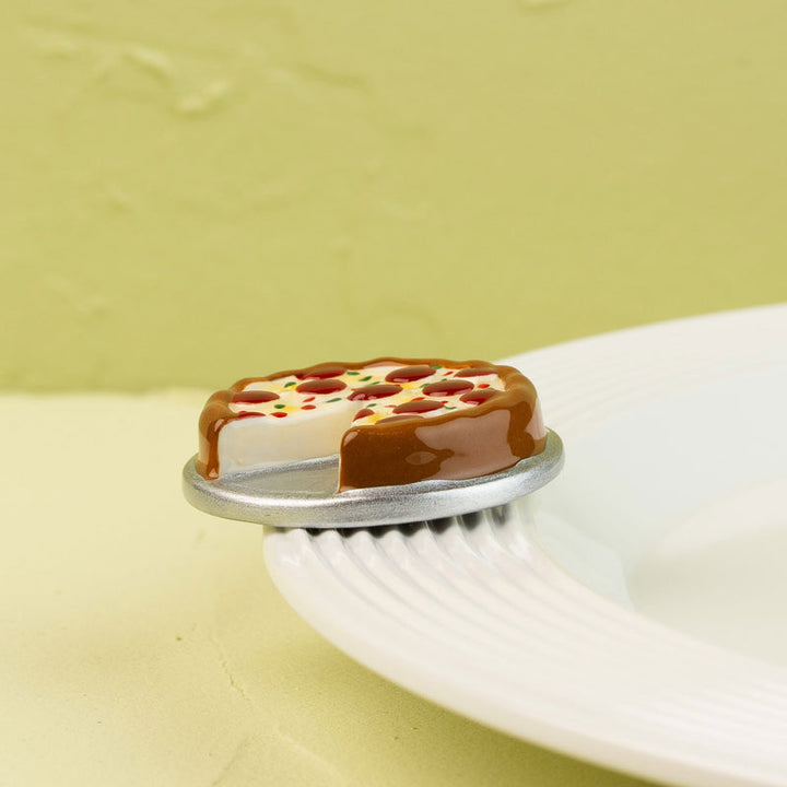 Nora Fleming Slice, Slice, Baby! hand-painted pizza slice mini displayed on a white serving plate.
