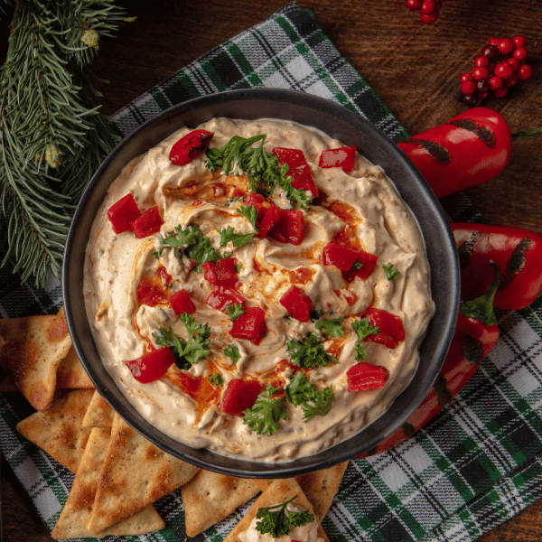 Wind &amp; Willow Roasted Red Pepper Dip Mix packet next to a bowl of creamy orange dip garnished with fresh red peppers and crackers.